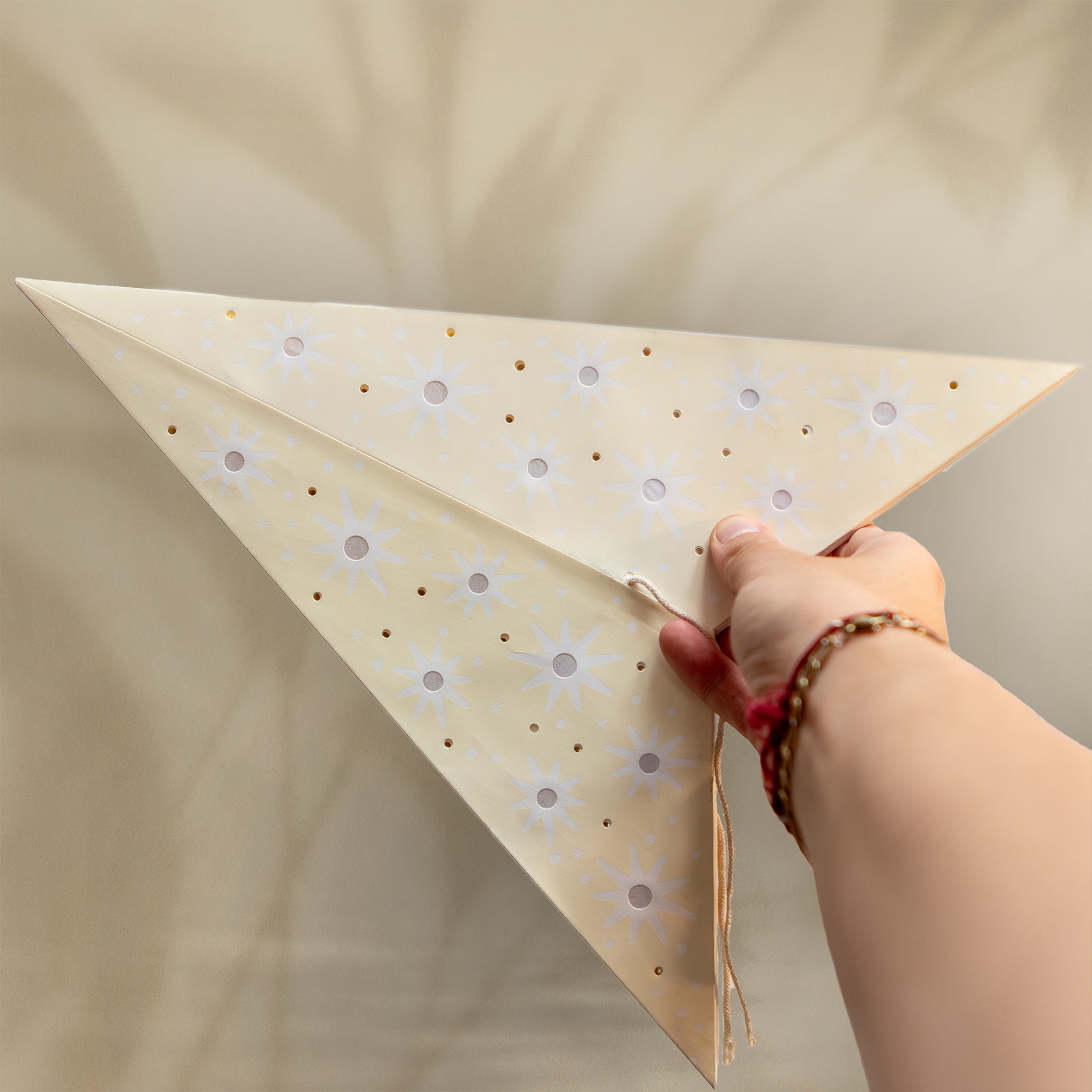 Hand holding a decorative triangle with floral patterns against a beige background
