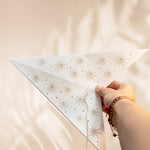 Hand holding a white triangular kite with star patterns against a beige background