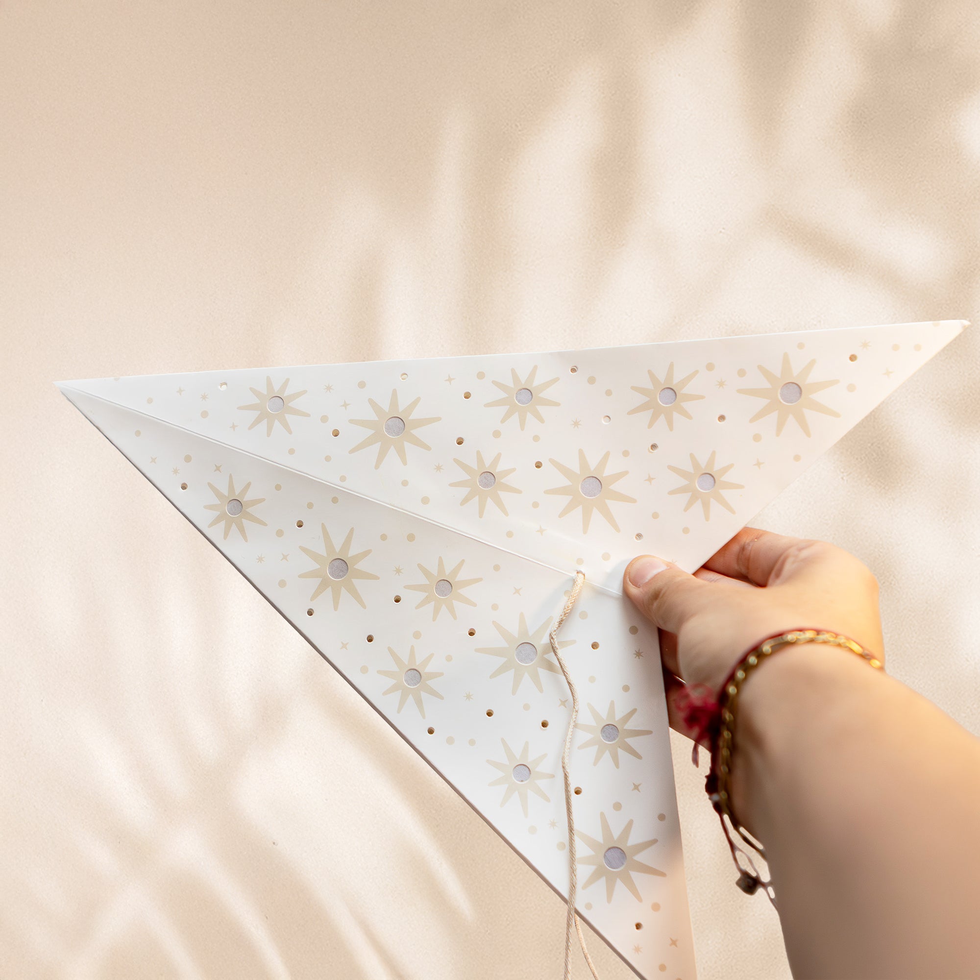Hand holding a white triangular kite with star patterns against a beige background