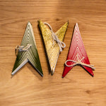 Three triangular wooden ornaments or cards in green, gold, and red, arranged side by side on a light brown wooden surface.