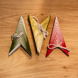 Three triangular wooden ornaments or cards in green, gold, and red, arranged side by side on a light brown wooden surface.