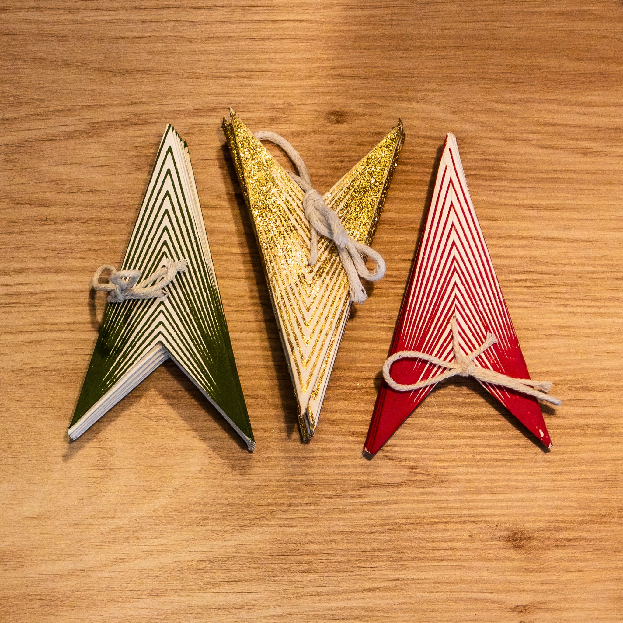 Three triangular wooden ornaments or cards in green, gold, and red, arranged side by side on a light brown wooden surface.