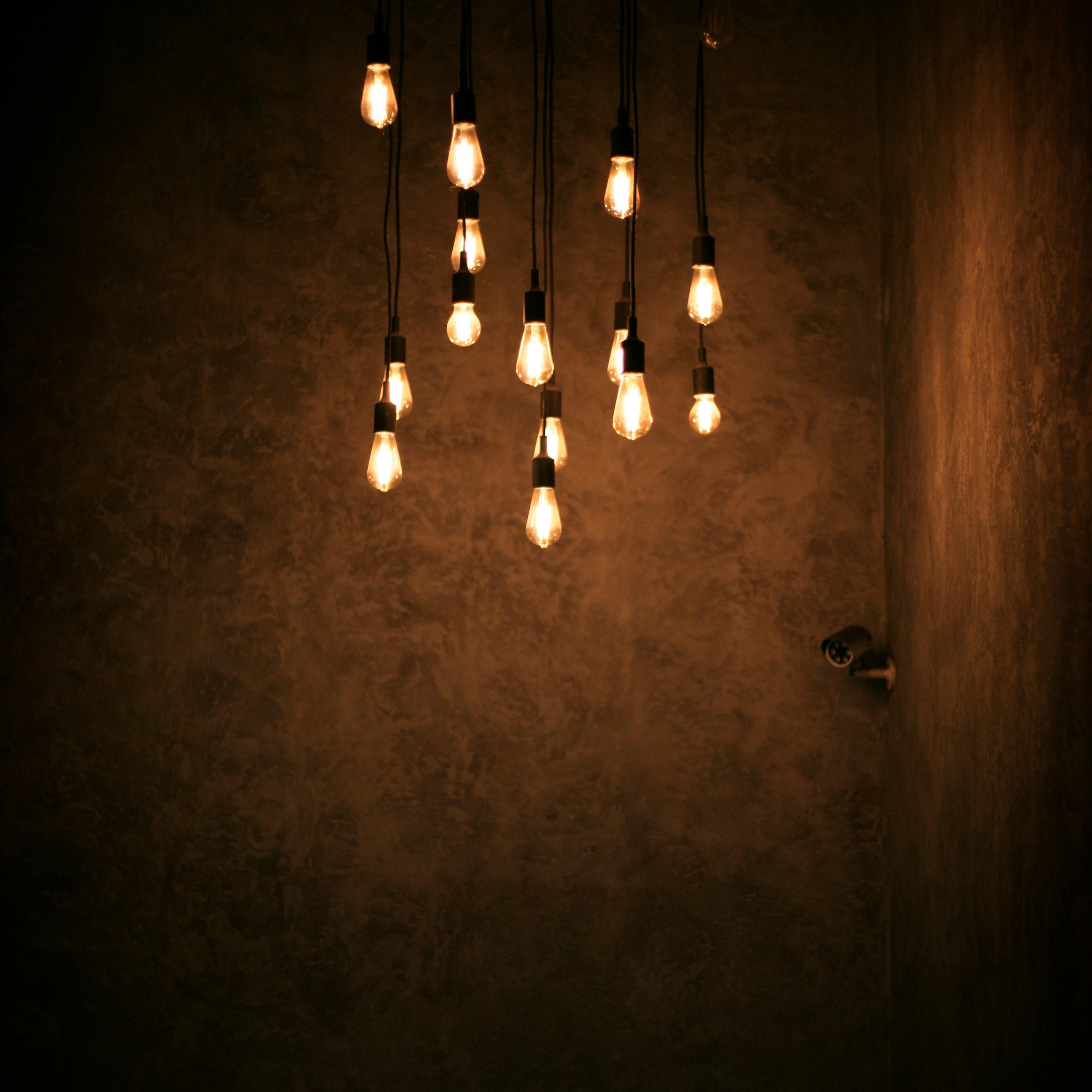 Cluster of hanging light bulbs casting a warm glow on a textured wall.