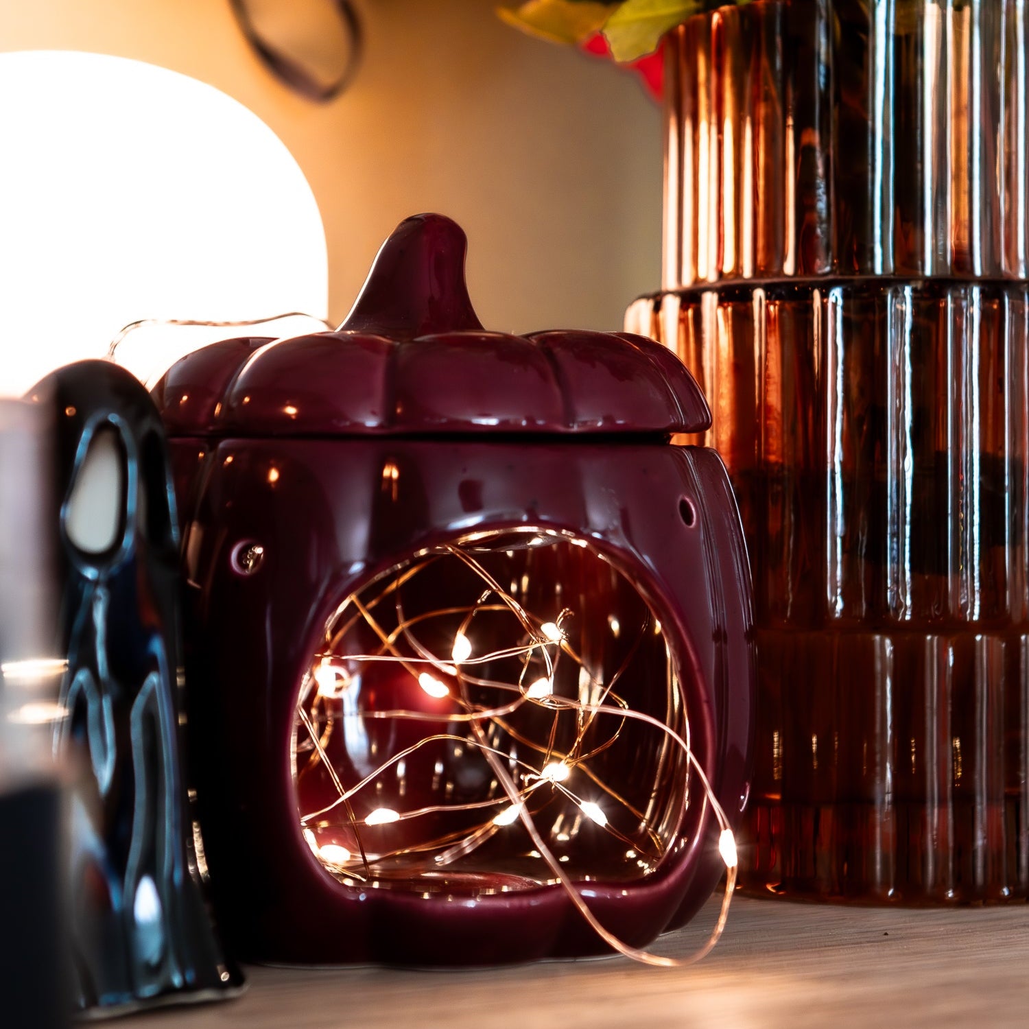 Decorative pumpkin-shaped lantern with string lights on a table, next to a vase with flowers.