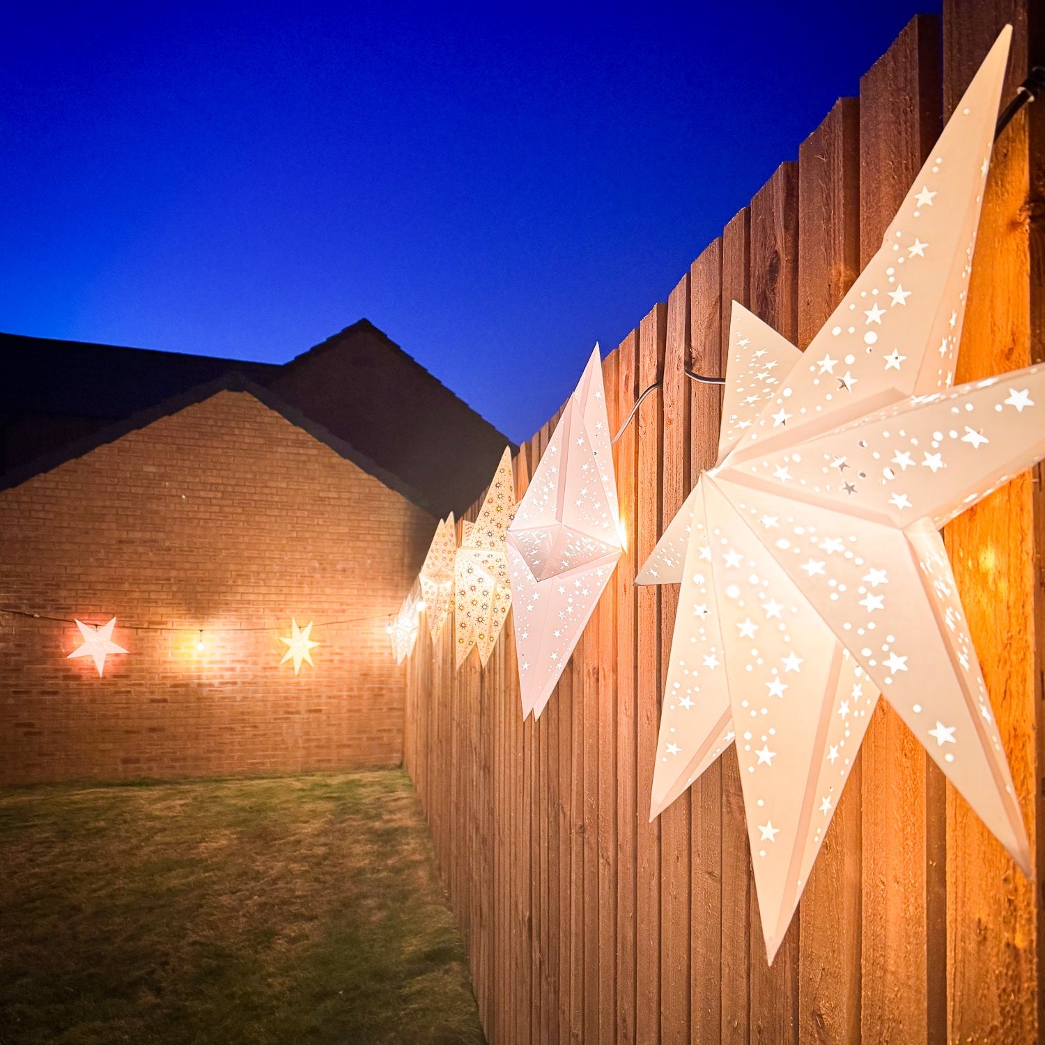 Decorative star lights on a wooden fence with a clear blue sky.