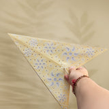 Hand holding a yellow triangle with floral pattern against a beige background