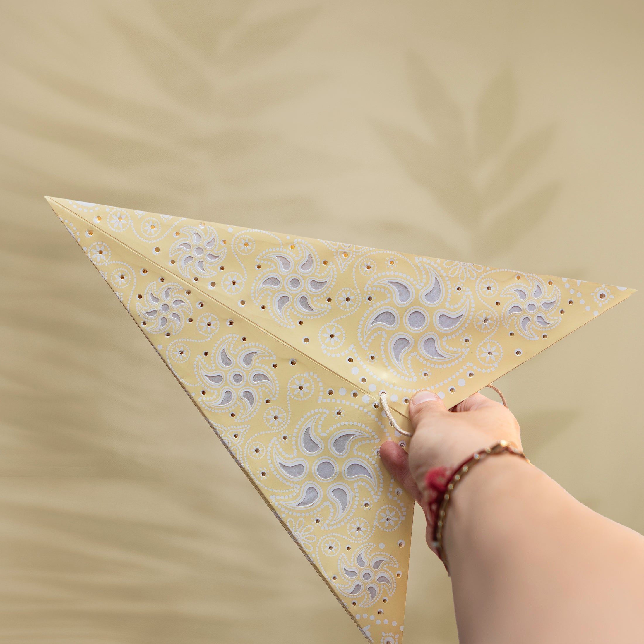 Hand holding a yellow triangle with floral pattern against a beige background