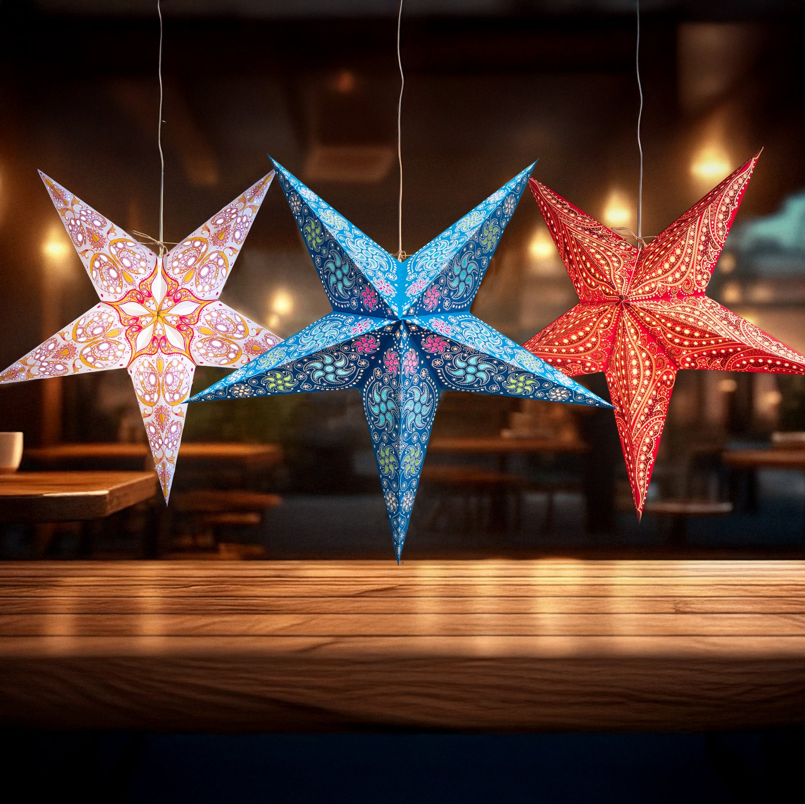 Three colorful star-shaped lanterns hanging above a wooden table with a blurred indoor background.
